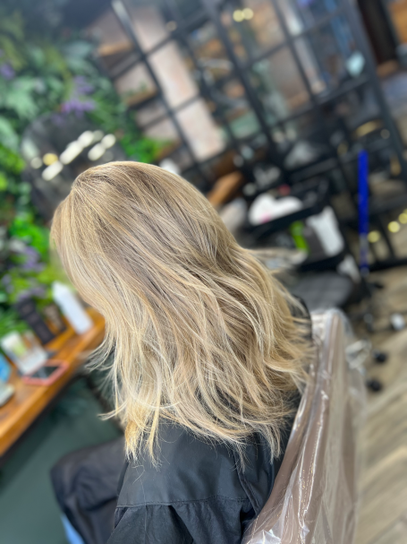 Woman with long, wavy blonde hair highlights sitting in a salon chair.