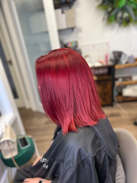 A woman with shoulder-length red hair sitting in a salon chair.