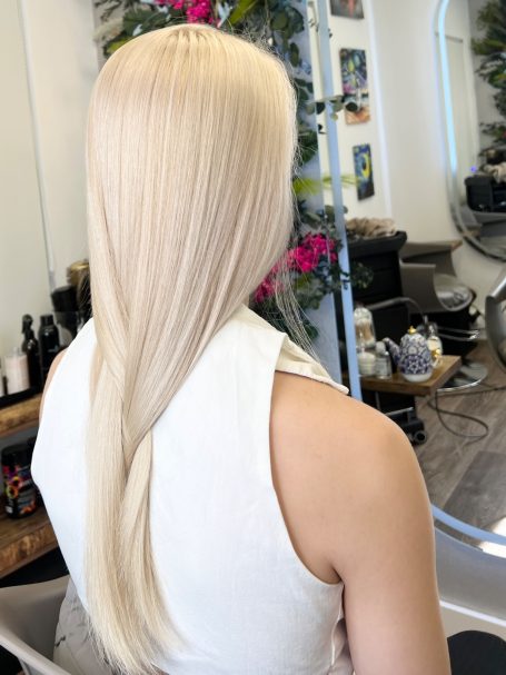 Long, straight, blonde hair viewed from behind, styled in a salon setting.